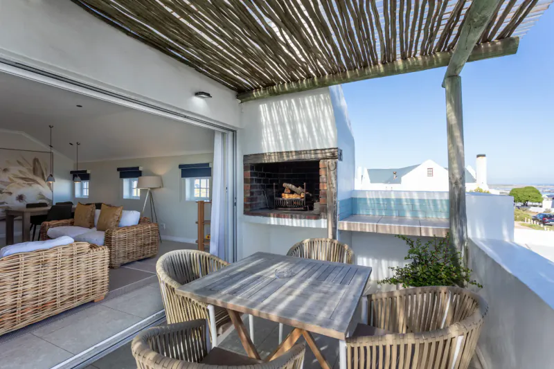 Spacious Oyster Suite balcony at Abalone Hotel with lit braai, rattan dining table, lounge chairs, ocean view.