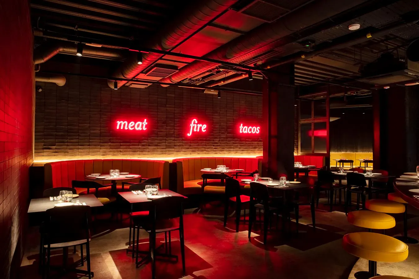 Vibrant red-lit interior of Temper smokehouse restaurant with 'meat fire tacos' neon sign, brick walls, bar seating, and tables.
