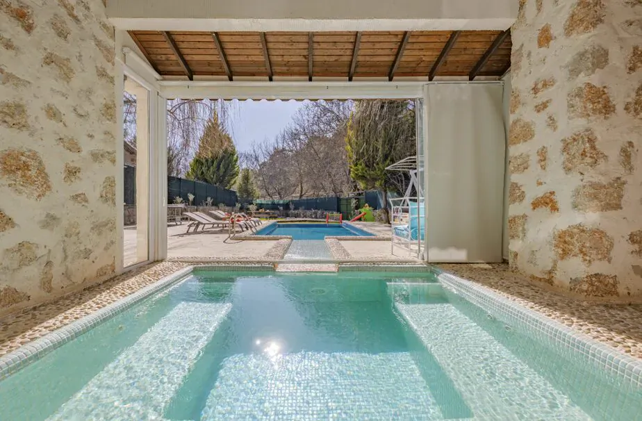 Stone archway view of luxurious infinity pool and spa with turquoise water, lounge chairs, and garden beyond.