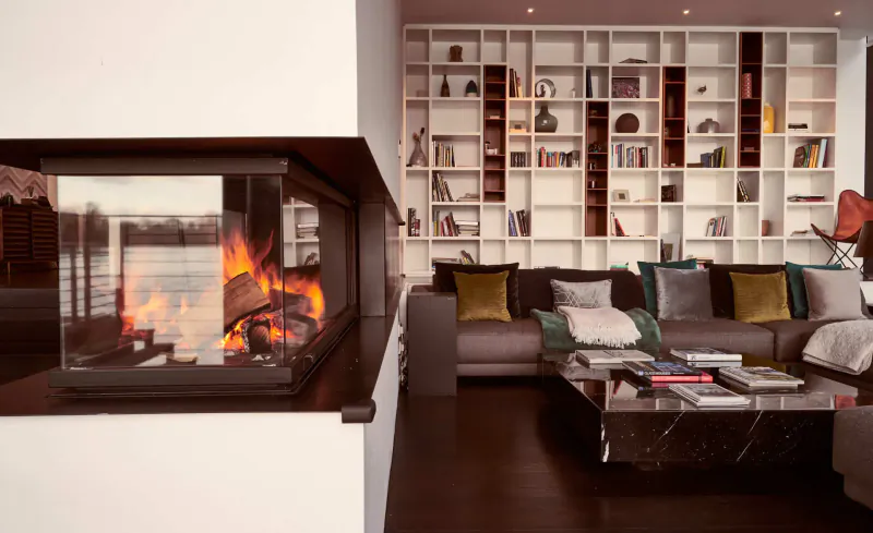 Modern living room with burning glass fireplace, white bookshelves, gray sofa, yellow pillows, and marble coffee table