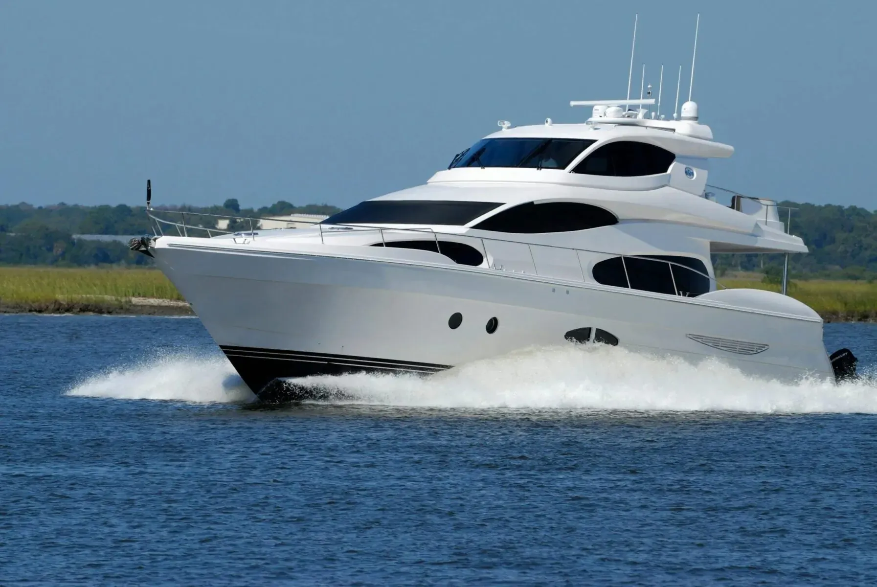 White luxury multi-deck yacht speeding across calm blue waters near marshy shoreline