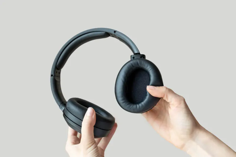 Hands holding open black Edifier W820NB wireless headphones, showcasing cushioned ear cups on gray background