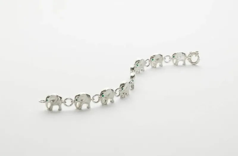Silver chain bracelet with linked elephant charms featuring green gem eyes
