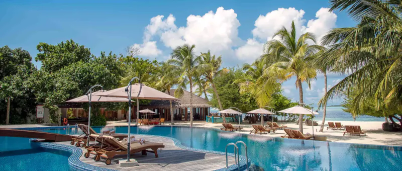 Hideaway Beach Resort & Spa, Maldives: infinity pool with loungers, umbrellas, palms, and ocean under blue sky