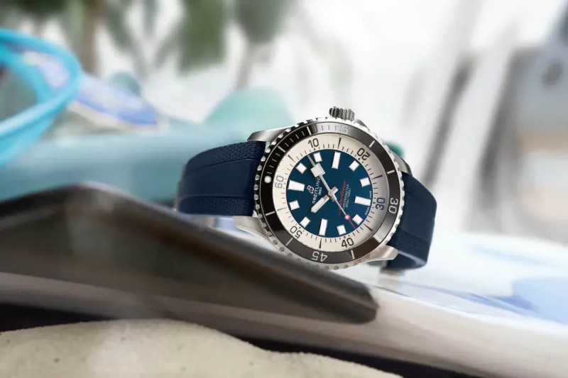 Tudor Superocean dive watch with blue rubber strap on sandy beach towel near ocean waves