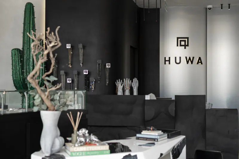 Huwa men's jewellery flagship store interior in Cairo: black decor, tall cactus, display cases with jewelry and gloves, logo on wall.
