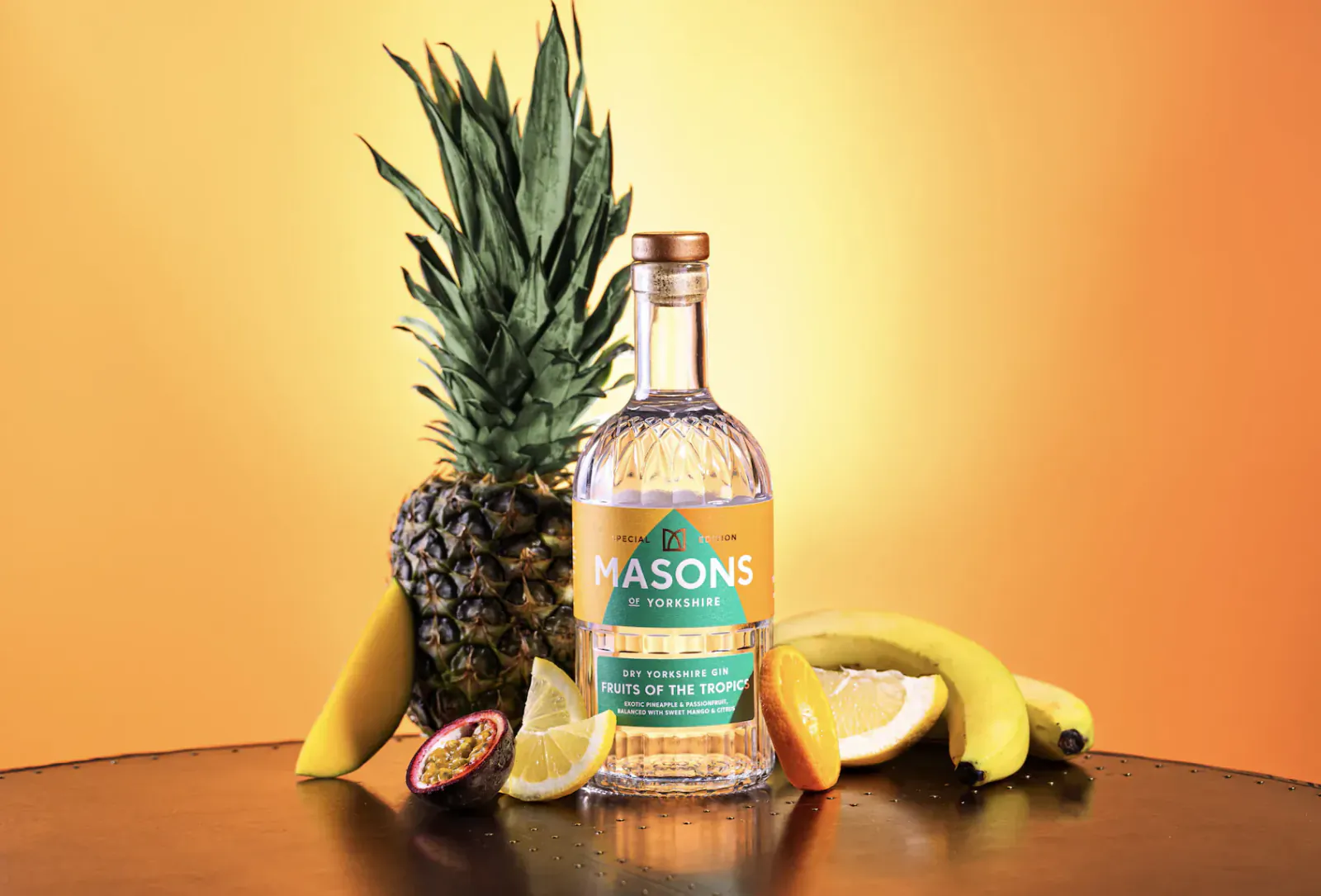 Masons of Yorkshire Tropical Yorkshire's First Gin bottle with pineapple, bananas, passion fruit, and lemon on orange background
