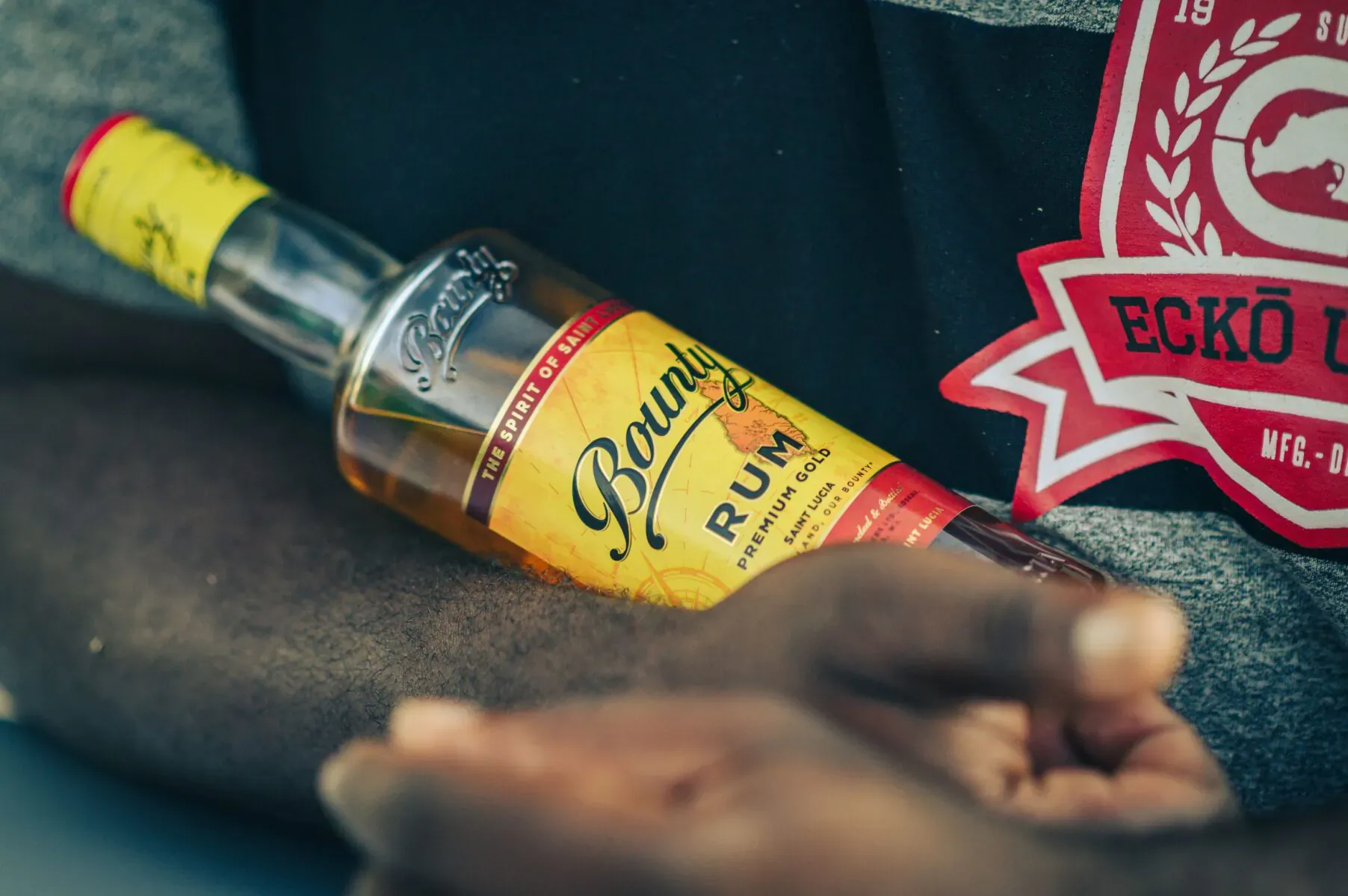 Bounty Rum bottle held in dark hand on black clothing with red Ecko Unltd patch, Bounty Rum label visible.