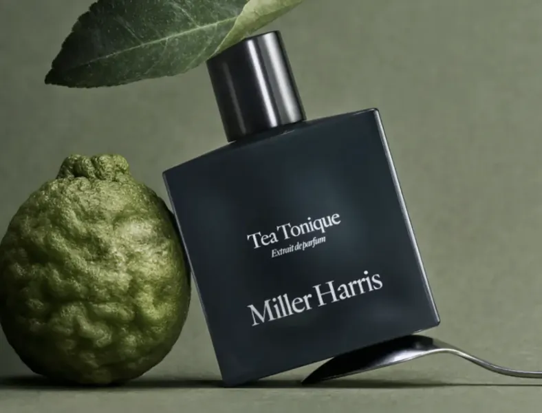Black Miller Harris 'Tea Tonique' eau de parfum bottle with green kaffir lime leaf and lime on green surface with spoon.