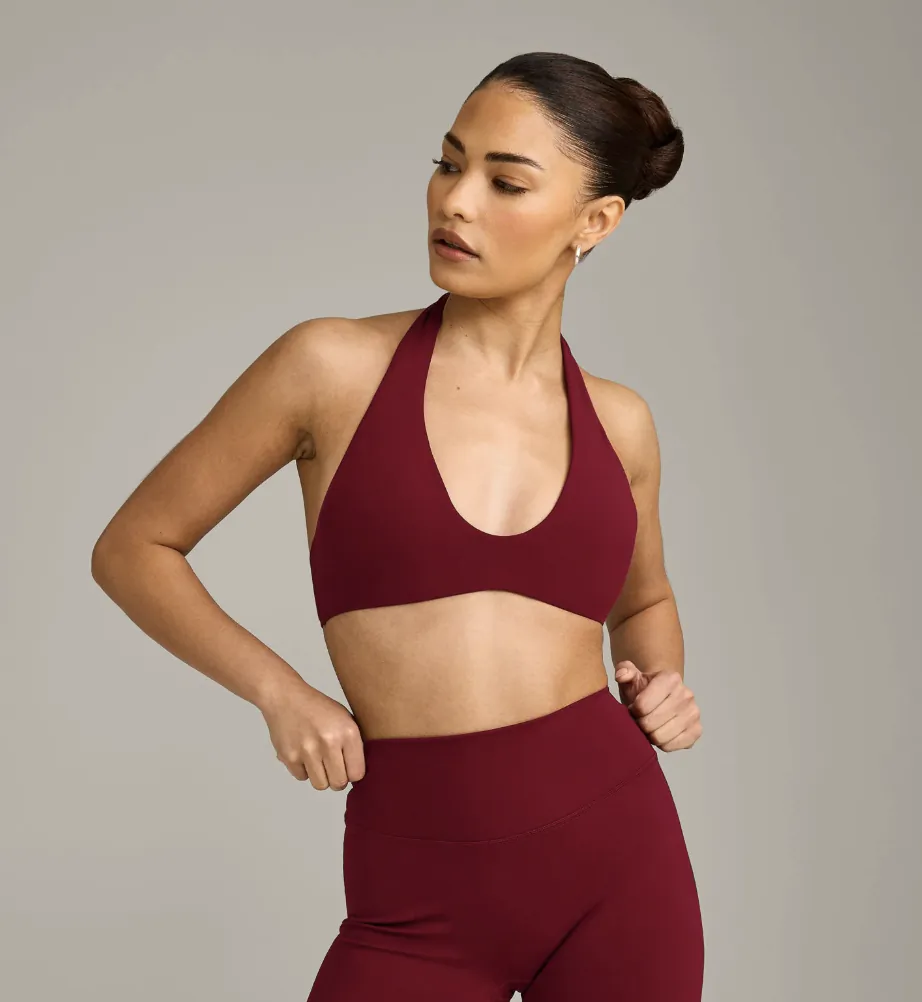 Woman with bun hairstyle modeling deep red halter crop top and high-waisted leggings, standing pose on gray background