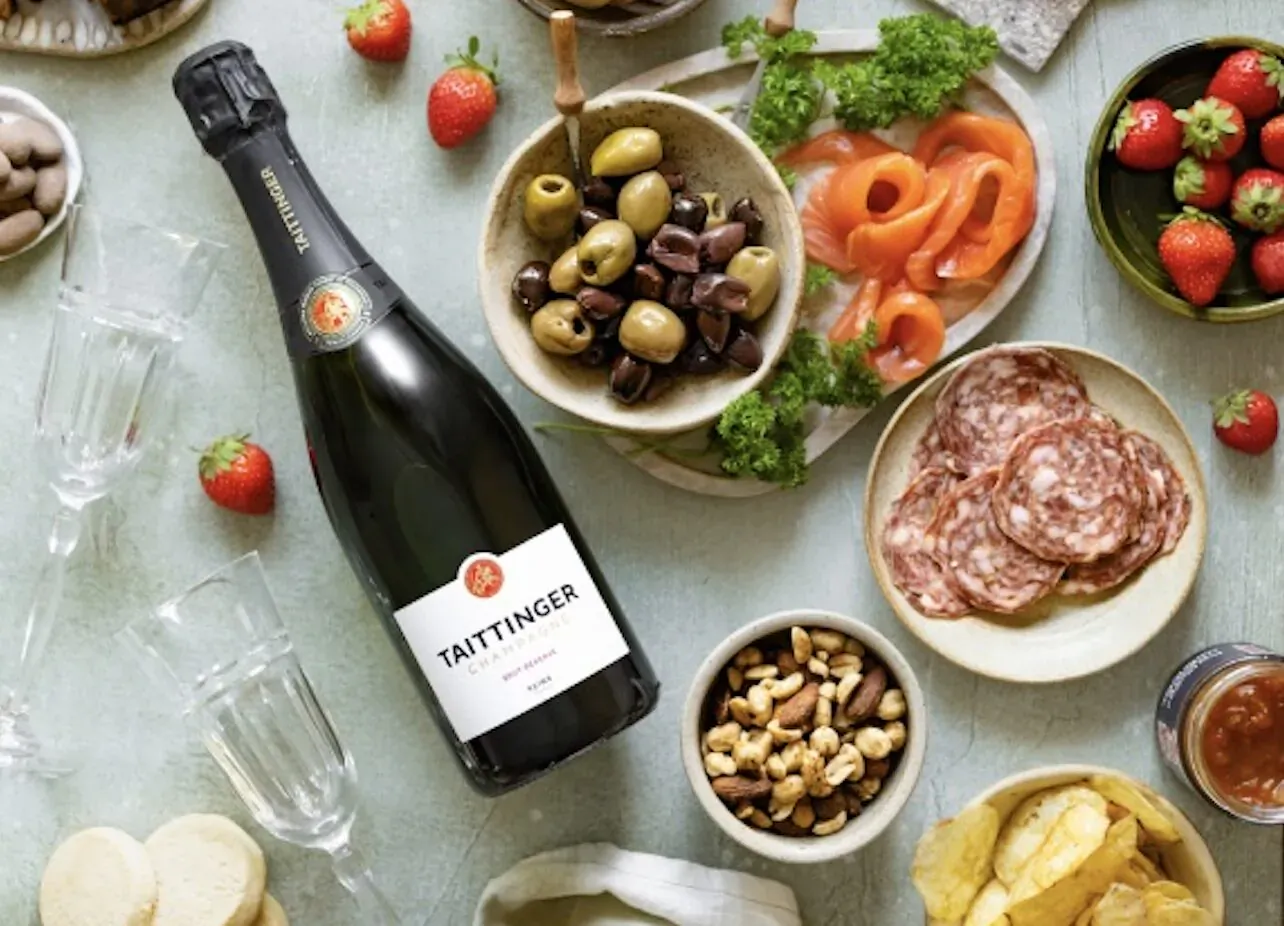 Taittinger champagne bottle with strawberries, olives, salami, nuts, crisps on table for Valentine's hamper