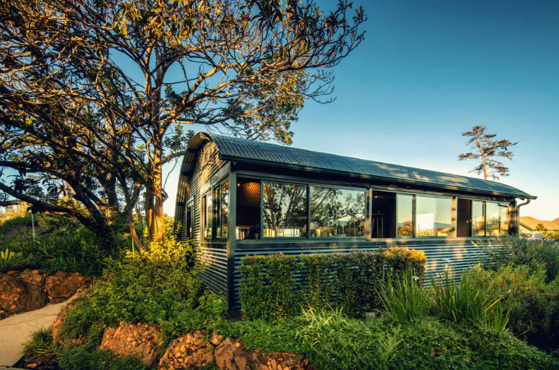 Modern corrugated metal Sky Villa at Cape Summer Villas, surrounded by lush gardens and trees under blue sky.