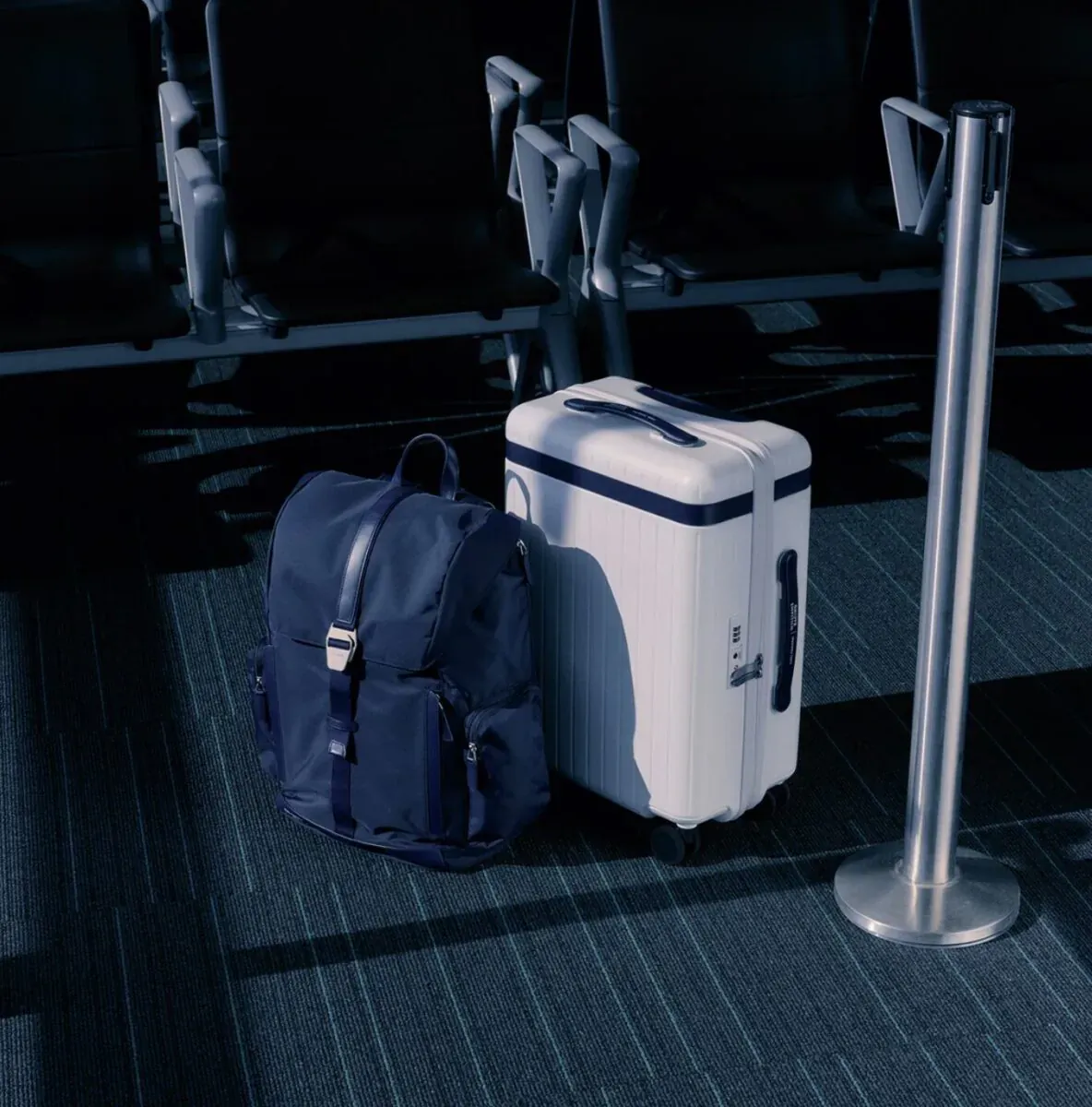 Navy Carl Friedrik backpack and white suitcase beside airport security stanchion.