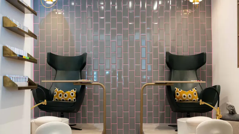 Modern pedicure station in Urban Retreat London City spa with green chairs, pink pillows, gray subway tile wall, and gold accents.
