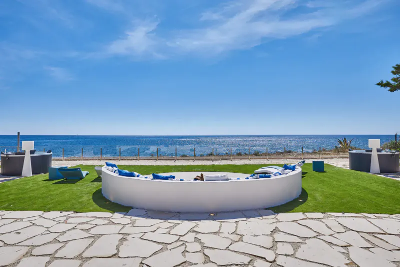 Circular white outdoor sofa with blue cushions and fire pit on green lawn, ocean view, luxury hotel terrace in Sicily