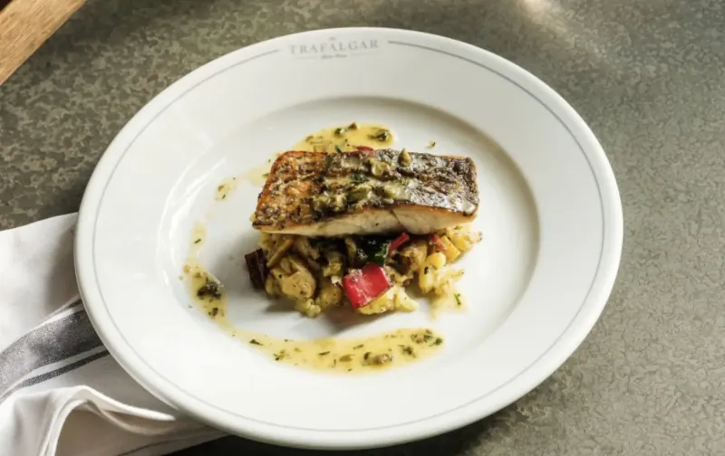 Seared sea bass fillet with herb sauce and couscous on white plate at Trafalgar Public House