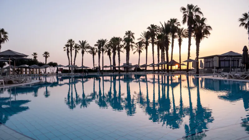 Sunset over Hilton Malta resort infinity pool reflecting palm trees and umbrellas on the Mediterranean beachfront