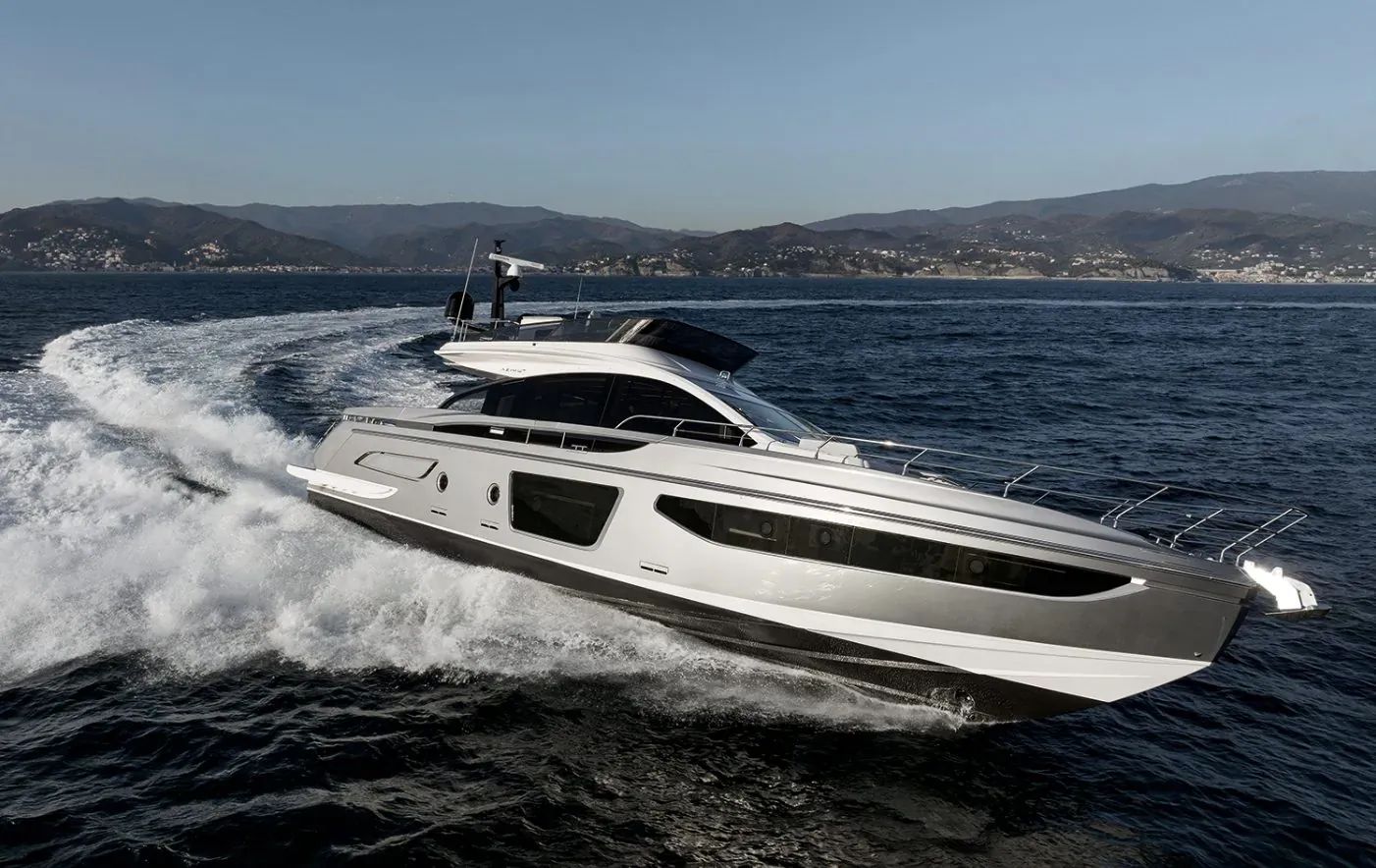Sleek silver Azimut yacht speeding through blue waters with coastal mountains in background