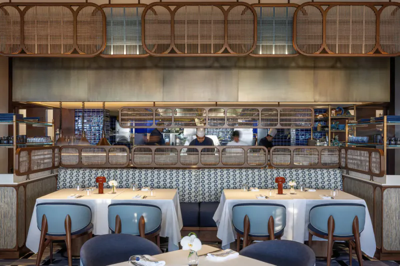 Elegant Sea Fu restaurant at Four Seasons Dubai: open kitchen with chefs, wooden accents, blue chairs, white tables, red flowers.