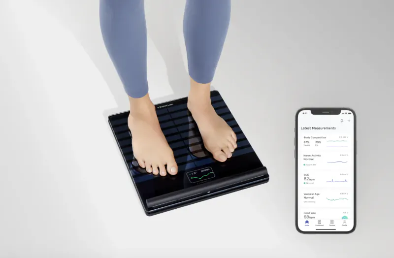 Woman standing barefoot on black smart scale, iPhone app displaying weight, BMI, and body fat metrics beside it.