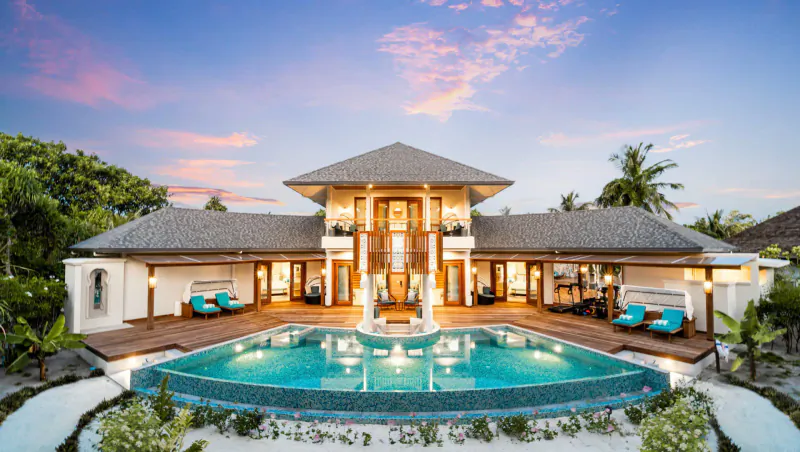 Luxurious multi-level beachfront villa at Hideaway Beach Resort, Maldives, with infinity pool, palms, and sunset sky.