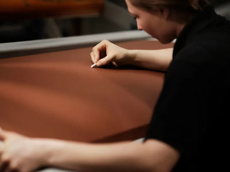 Worker in black shirt delicately hand-stitching brown leather on Rolls-Royce Arcadia Droptail interior