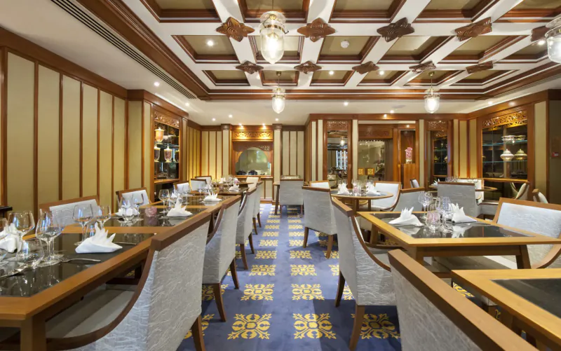 Elegant Nipa Thai restaurant dining room with wooden beamed ceiling, ornate lamps, and neatly set tables.