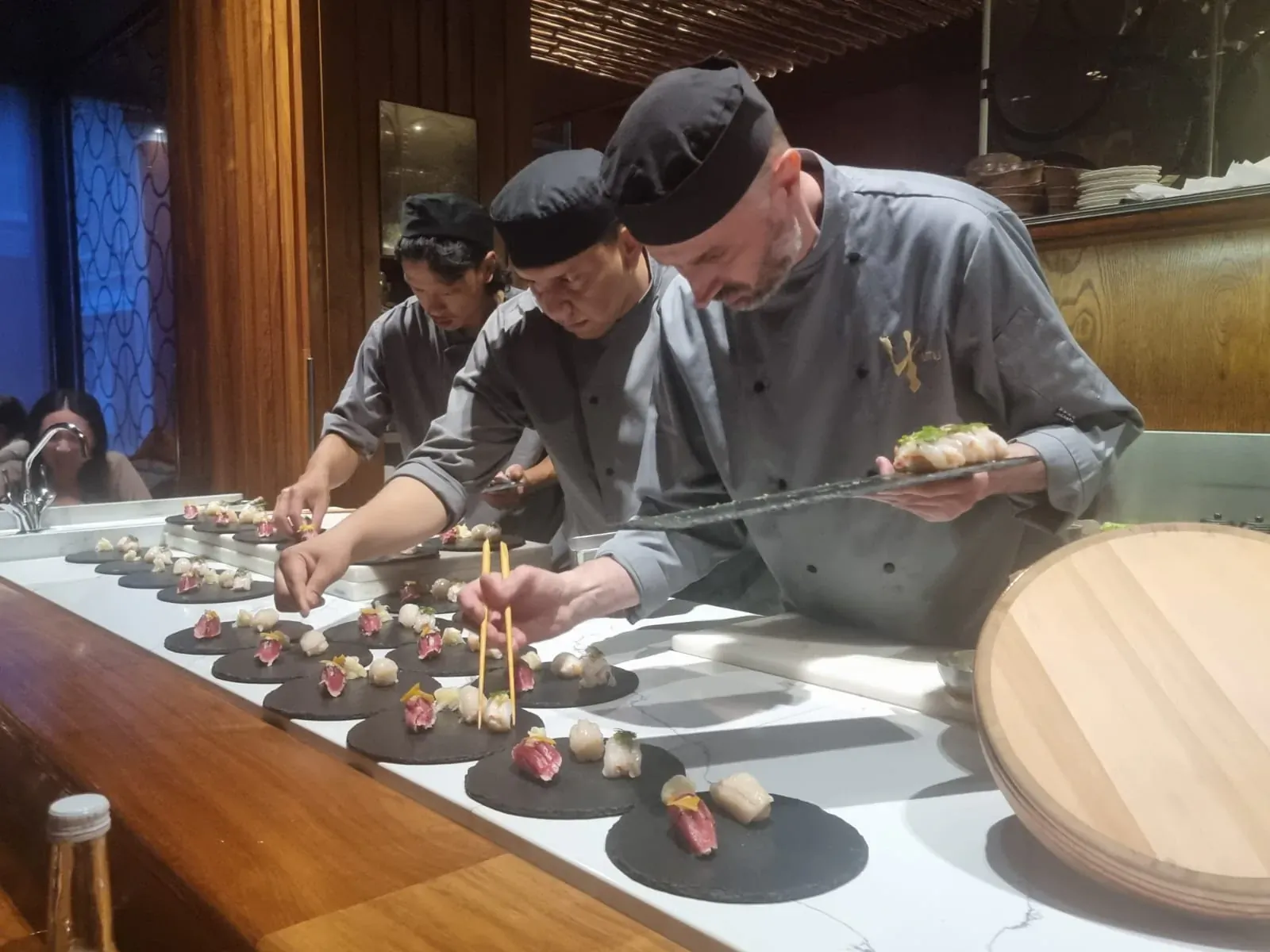 Chefs in UMU kitchen plating sushi and sashimi on black dishes at wooden counter