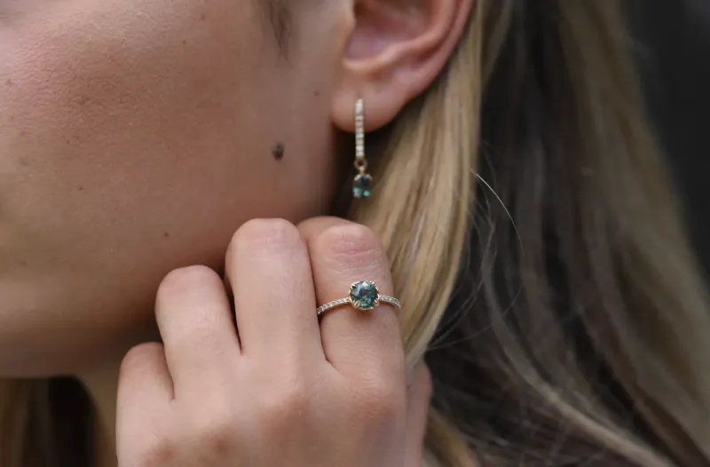 Close-up of woman's hand with gold ring featuring green gemstone and matching drop earring