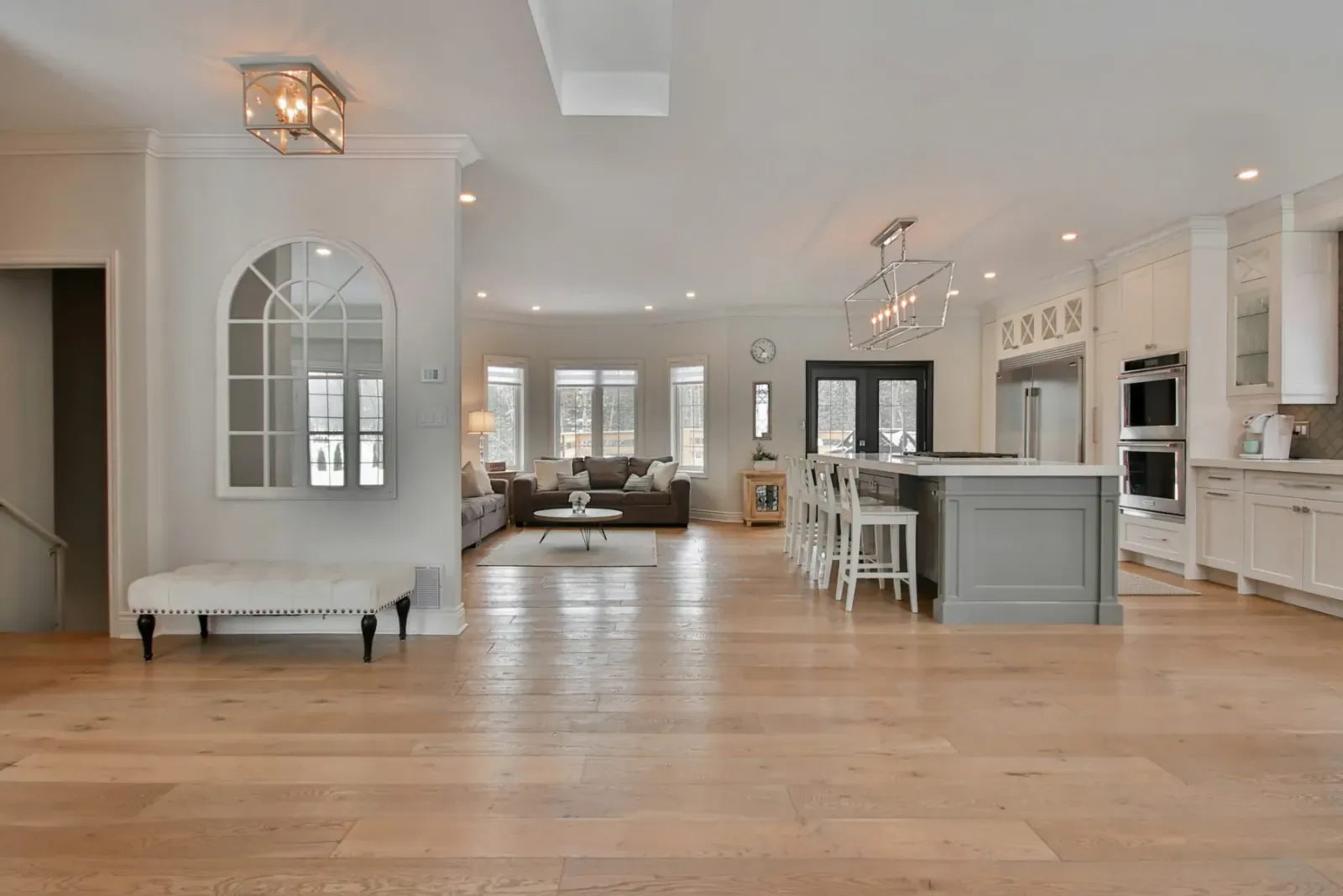 Spacious open-concept living room and modern kitchen with oak hardwood floors, white cabinets, and large island.