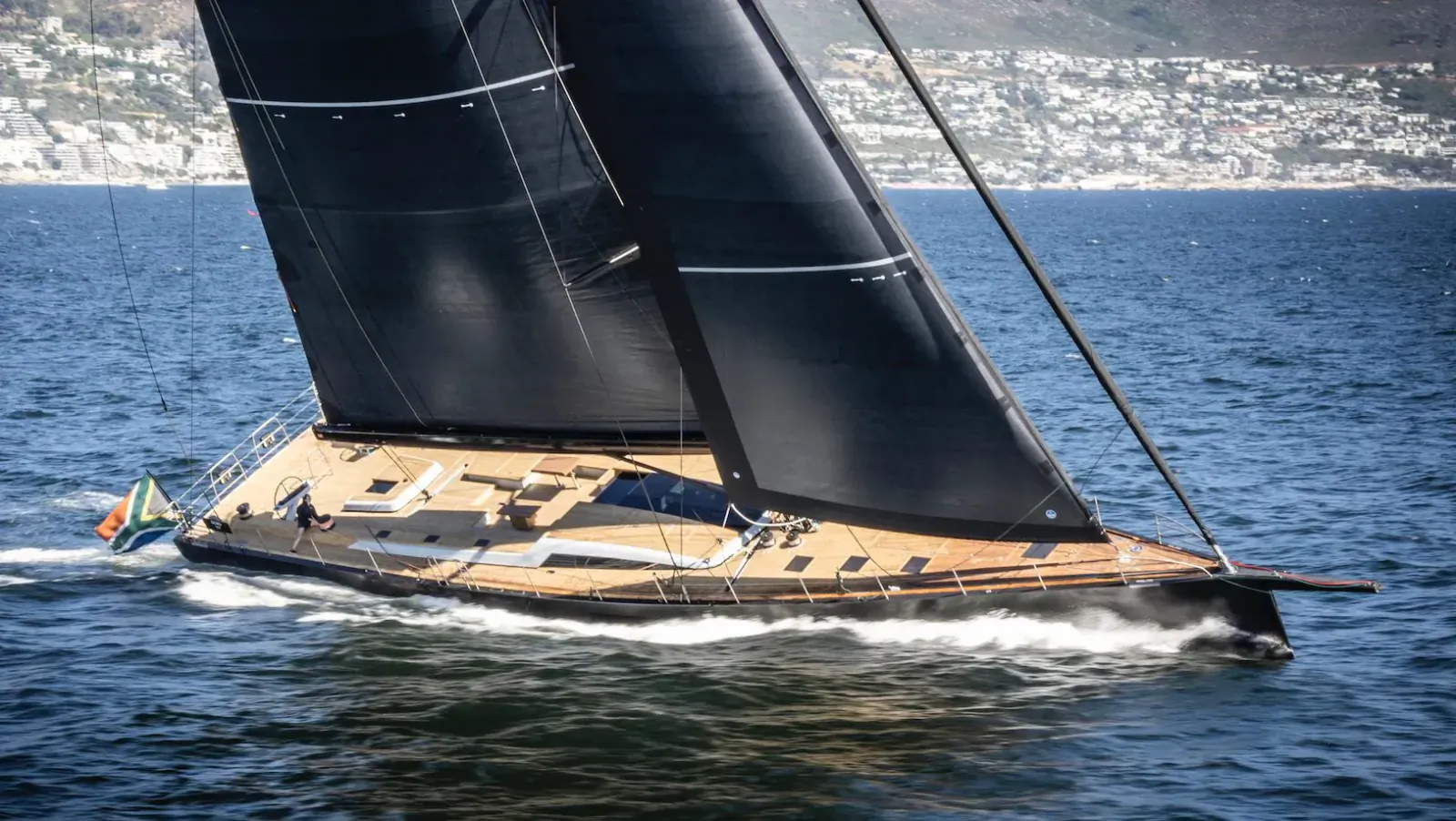 Sleek black-sailed yacht KIBOKO 4 with South African flag speeding on ocean near Cape Town mountains