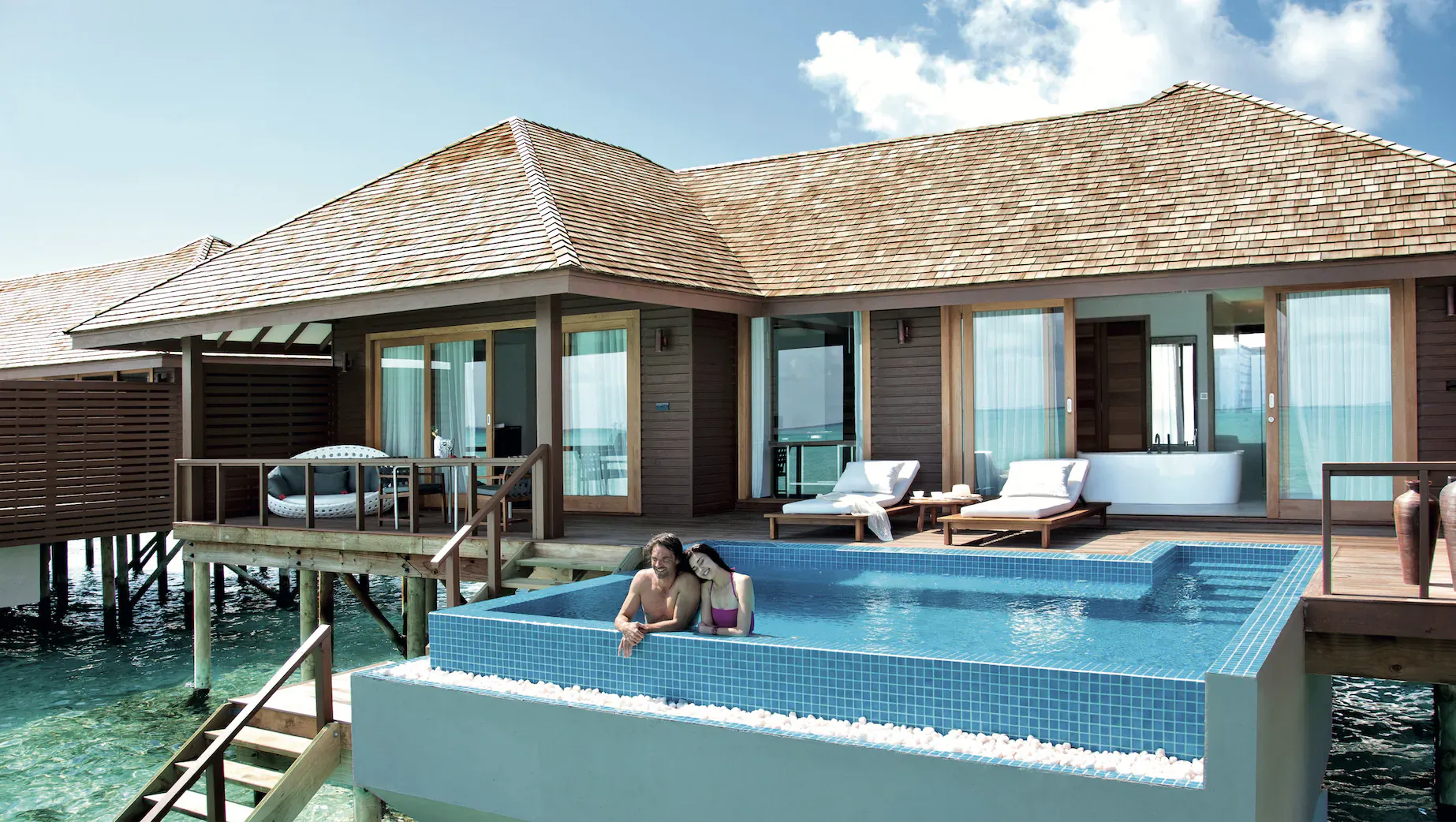 Couple relaxing in infinity pool of overwater villa at Hideaway Beach Resort, Maldives, with turquoise lagoon views