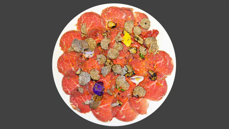 Plate of thinly sliced raw beef carpaccio topped with rare Italian truffles, capers, onions, and herbs