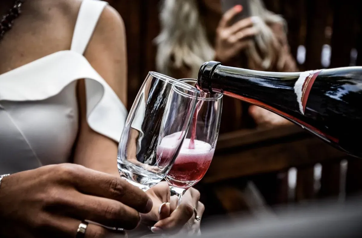 Close-up of woman in white dress pouring red wine from bottle into wine glass outdoors