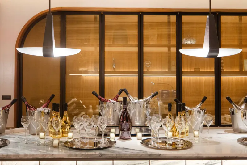Elegant event table with champagne bottles in ice buckets, glasses, and candles against modern wooden wall backdrop