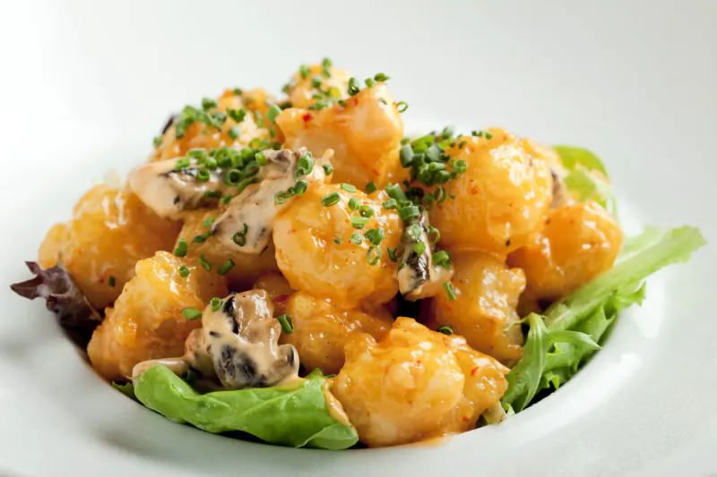 Close-up of creamy orange-sauced shrimp with chives and lettuce on white plate at Nobu