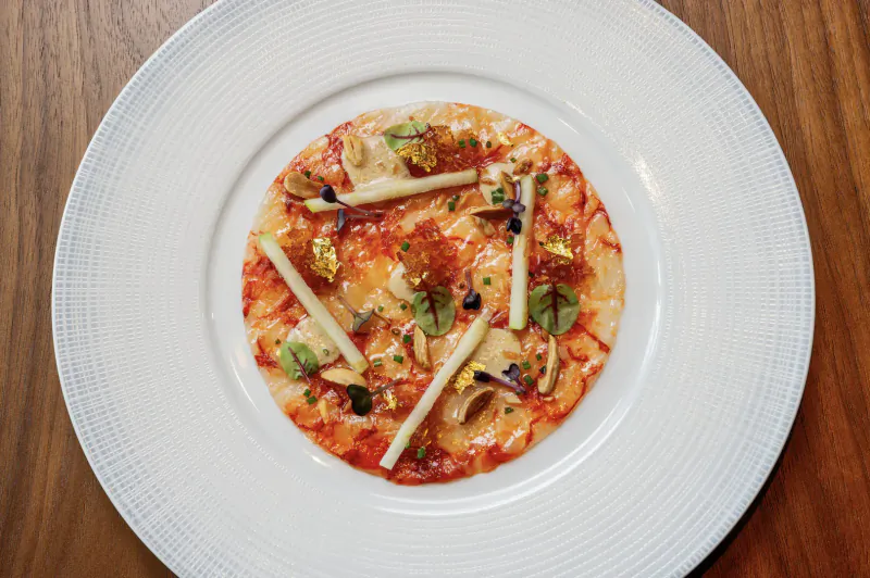 Close-up of Sea Fu dish: small pizza with tomato sauce, mushrooms, cheese, herbs on white plate atop wooden table