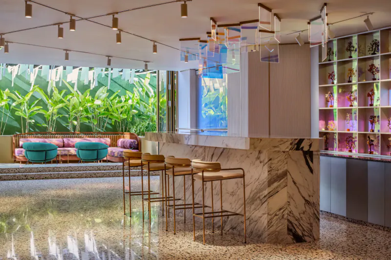 Modern hotel bar at Gem Forest Hotel, Nairobi: marble counter, turquoise stools, pendant lights, lush banana plants visible through windows.