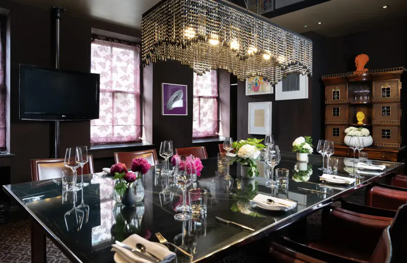 Elegant dining room for cooking masterclass at Pied à Terre: glossy black table set with wine glasses, flowers, chandelier, art.