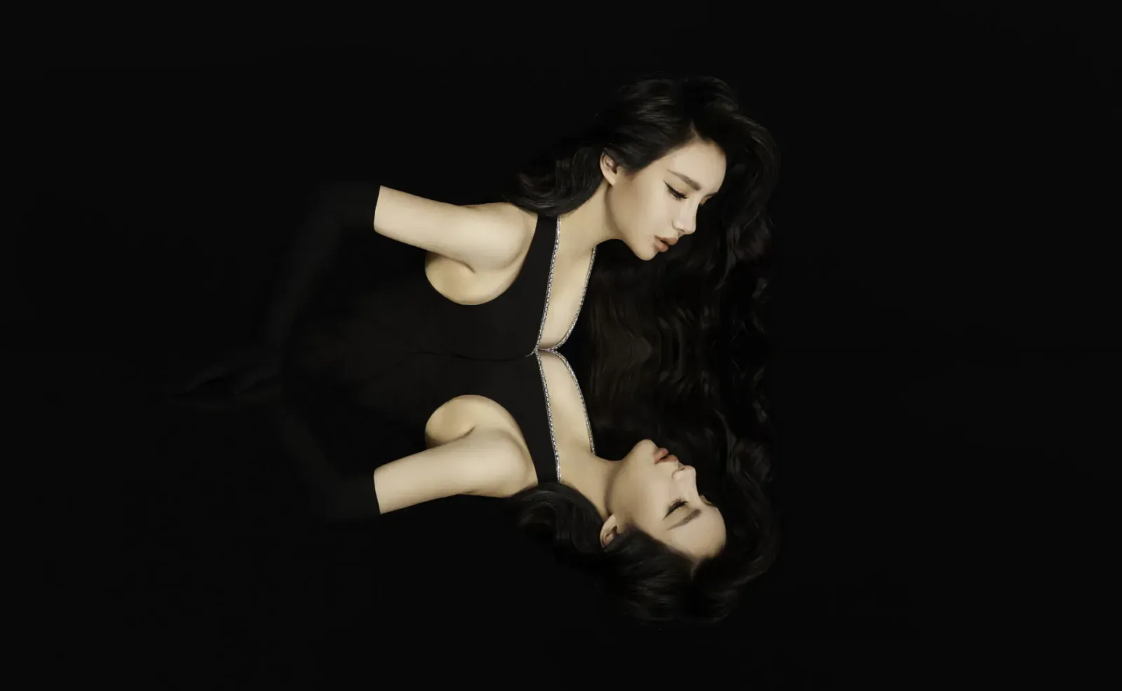 Emma Blunt in black sleeveless dress, mirrored reflection on dark background, elegant pose