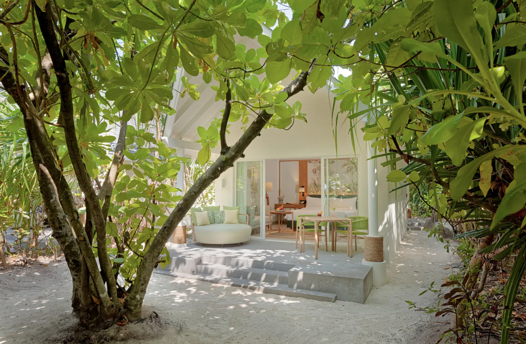 Amari Raaya Maldives luxury overwater villa with open glass doors, lush green trees, outdoor seating on sandy deck