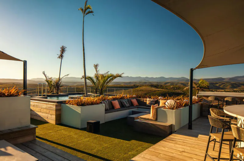 Sky Villa Boutique Hotel rooftop terrace with plush seating, infinity pool, potted palms, and mountain sunset views.