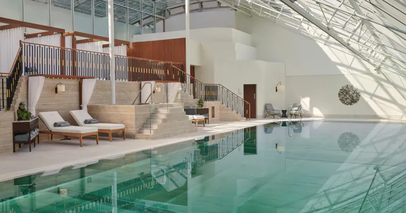 Luxurious indoor pool at Carlton Tower Jumeirah with sun loungers, wooden cabanas, and glass atrium ceiling