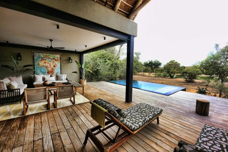 Luxurious outdoor deck at Monwana Game Lodge with lounge seating, infinity pool, world map art, and savanna view.